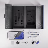 A professional dart set arranged in a top-down layout on a light gray background. The set includes a large black presentation box with custom foam inserts, a silver and blue patterned zippered carrying case, three darts, three tips, a black dartboard cover, a black keychain, and several small accessories.