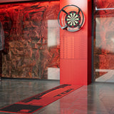 A red and black dartboard mat with the word 'TOR' printed on it, laid out on a gray tiled floor in front of a red LED wall and dartboard in a modern indoor setting.