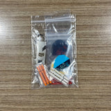 A clear plastic zip-top bag containing a small dart keychain set on a wood-grain tabletop. The set includes assorted dart Accessory Pack. Side B