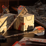 Darts with red and gray fletchings on a wooden surface with boxes in the background.